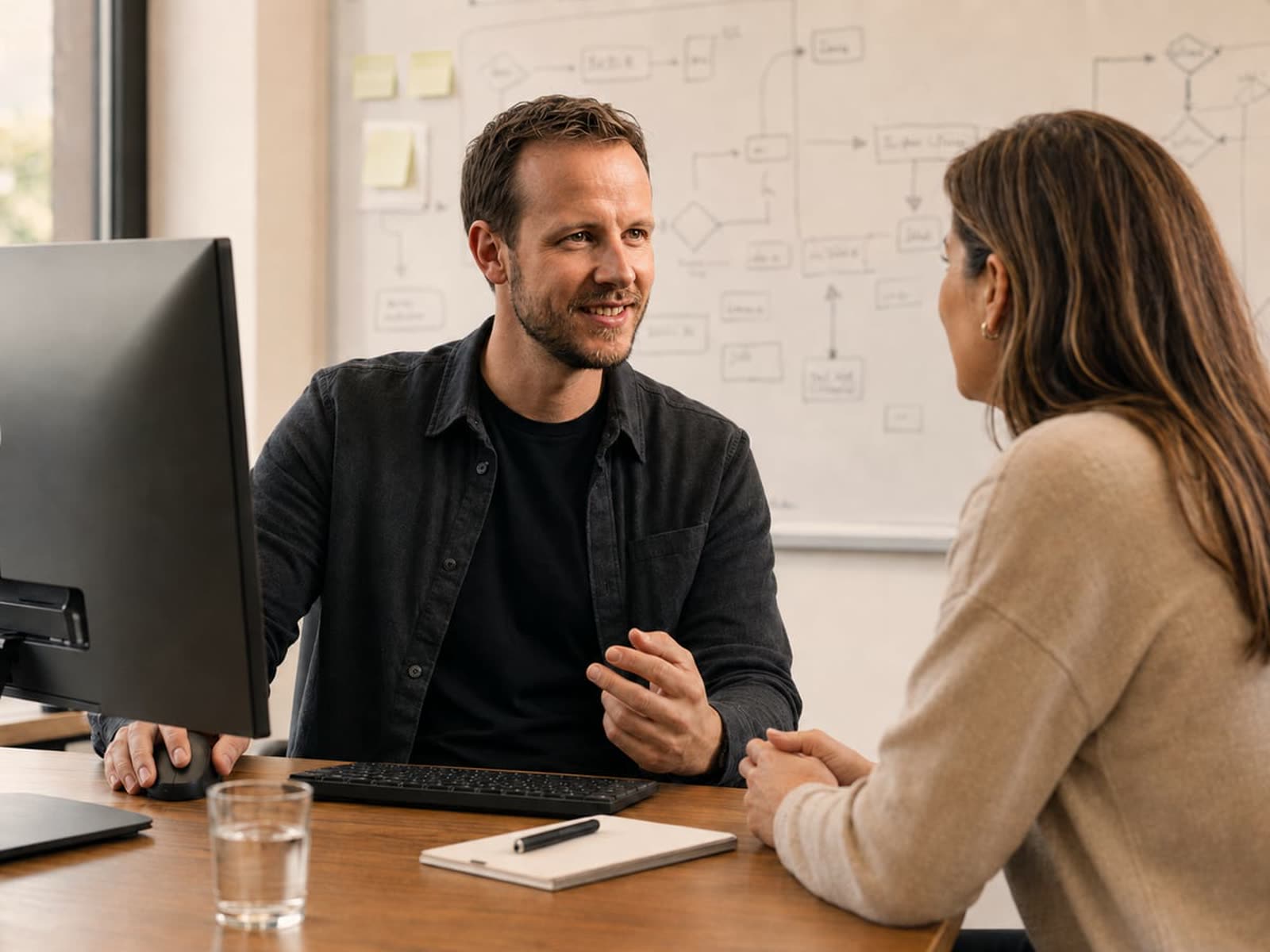 Twee mensen bespreken een uitgeprint processchema aan een tafel bij het raam